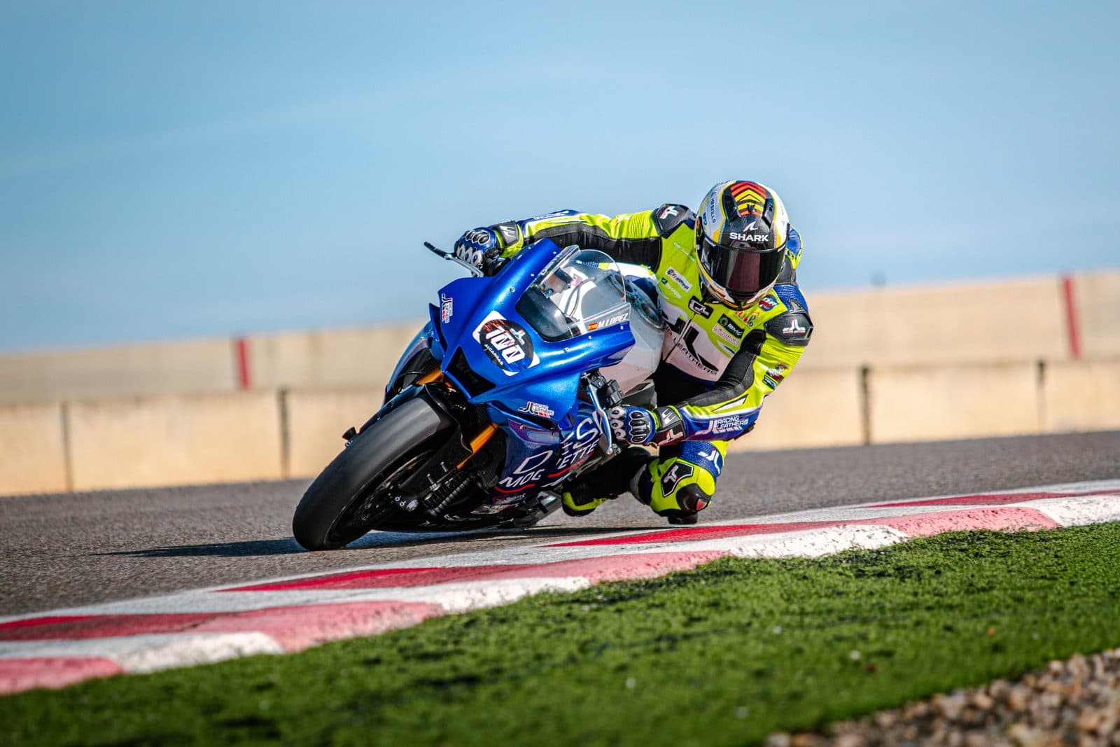 Pilote en combinaison jaune penché sur une moto bleue à la corde d'un virage, lors d'un roulage sur circuit